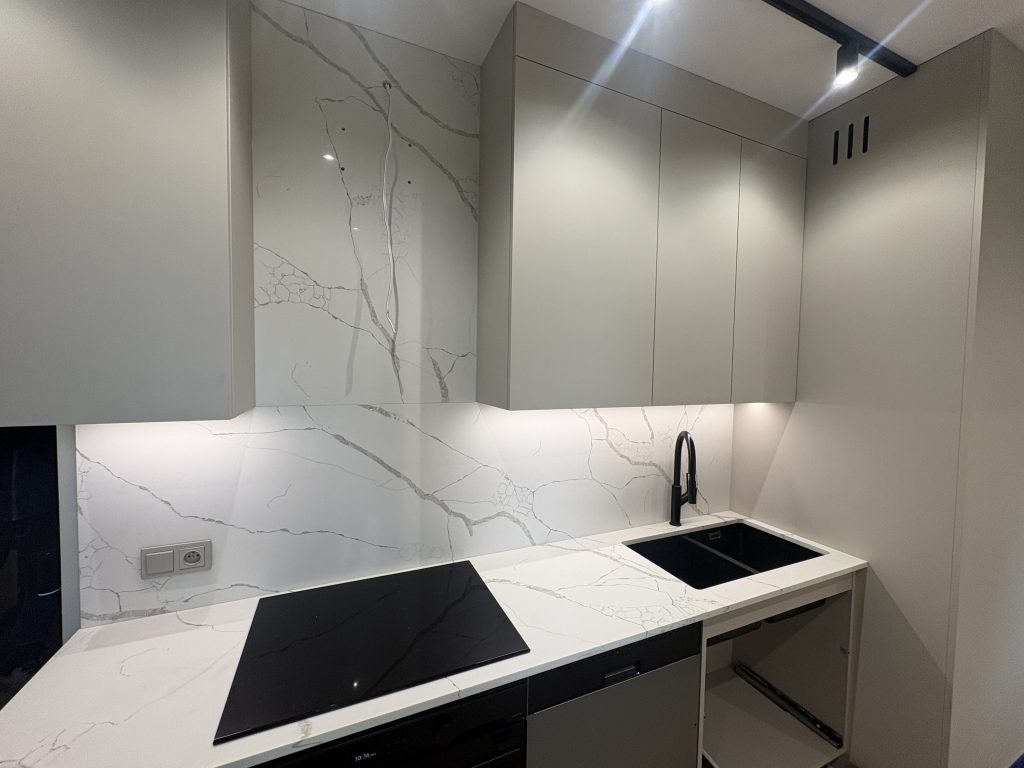 kuchnia wykończona konglomeratem kwarcowym Calacatta Silva - widok na blat z indukcją oraz zlewem i okładziną ścienną