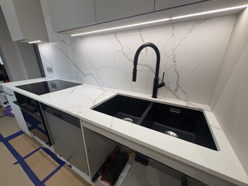 kuchnia wykończona konglomeratem kwarcowym Calacatta Silva - widok na blat ze zlewem i indukcją oraz okładzinę z prawej strony