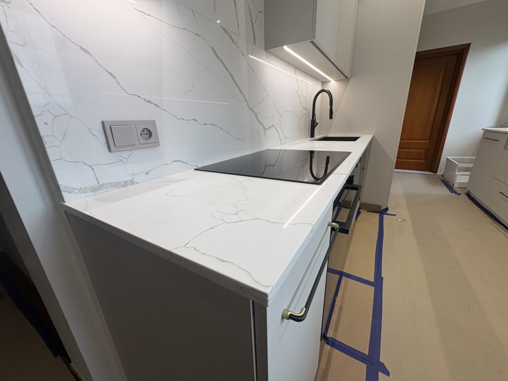 kuchnia wykończona konglomeratem kwarcowym Calacatta Silva - widok na blat z indukcją oraz zlewem i okładziną ścienną z lewej strony