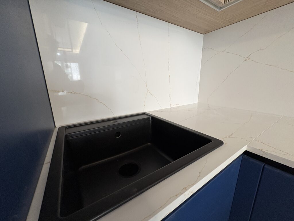 kuchnia wykończona blatami i okładzinami z konglomeratu Calacatta Gold - widok na zlew nakładany