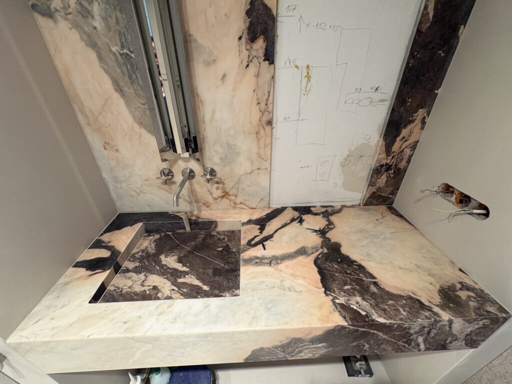 Łazienka wykończona marmurem Calcataa Nobile - blat ze zintegrowaną umywalką oraz okładziny ścienne do sufitu - widok z przodu