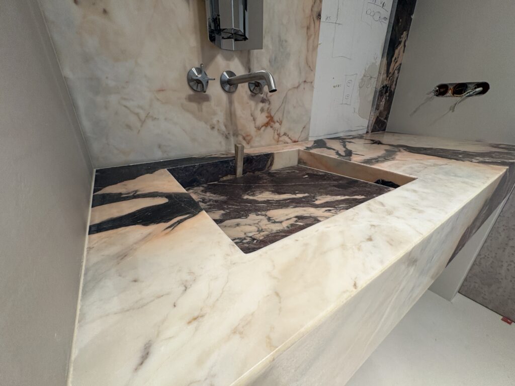 Łazienka wykończona marmurem Calcataa Nobile - blat ze zintegrowaną umywalką oraz okładziny ścienne do sufitu - widok z lewej strony