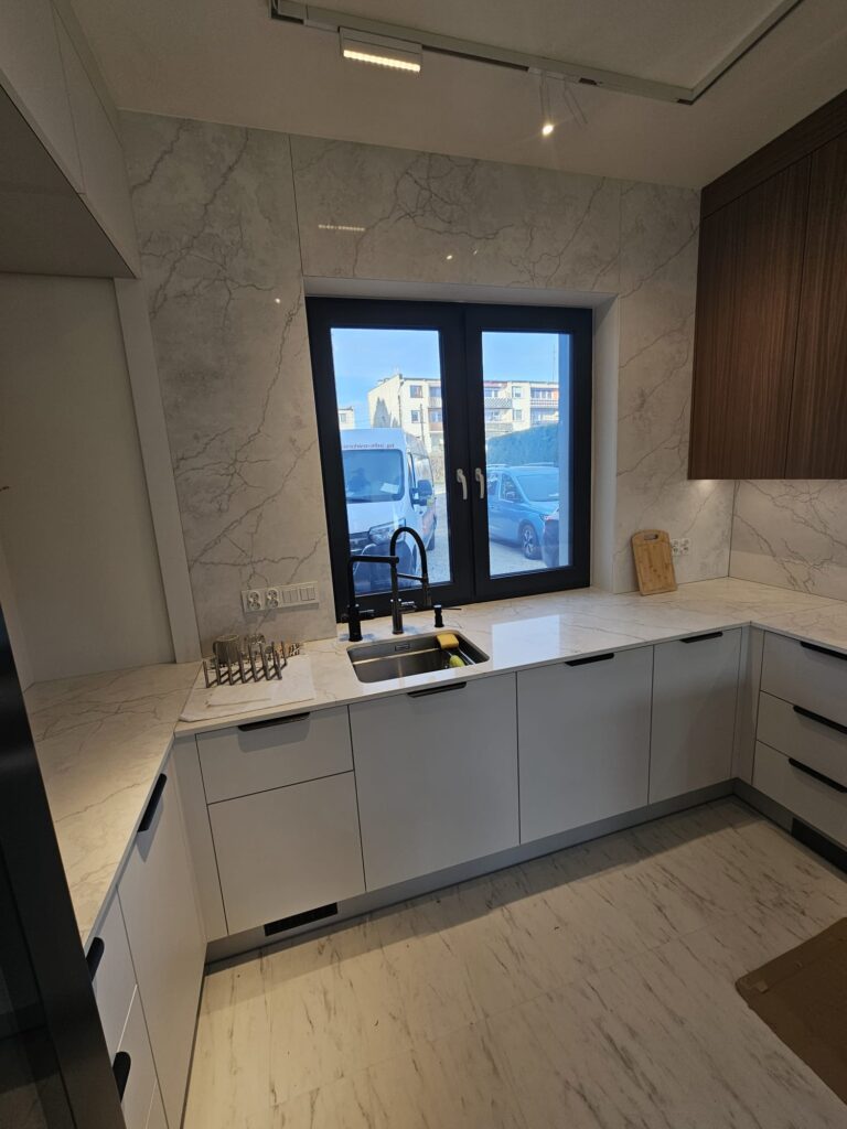 kuchnia wykończona blatami i okładzinami ściennymi z konglomeratu Calacatta Concorde - widok na okno z przodu