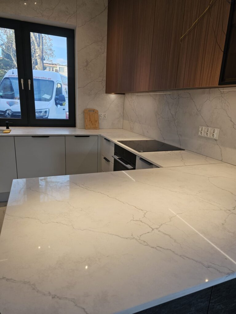 kuchnia wykończona blatami i okładzinami ściennymi z konglomeratu Calacatta Concorde - widok na całość z poziomu blatu na wyspie