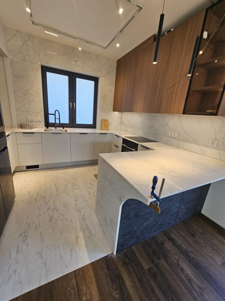 kuchnia wykończona blatami i okładzinami ściennymi z konglomeratu Calacatta Concorde - widok na całość z daleka